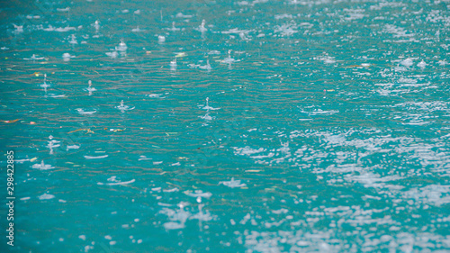 Raindrops on water surface of lake. The turquoise water of river. Rainy weather at sea