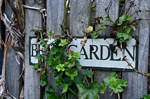 Beer garden sign on a paling fence, hand painted, overgrown with a trailing geranium and with rusty screws on the entrance to a country hotel's outdoor drinking area