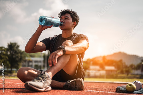 Fototapeta Naklejka Na Ścianę i Meble - The young man wore all parts of his body and drink water to prepare for jogging on the running track around the football field.