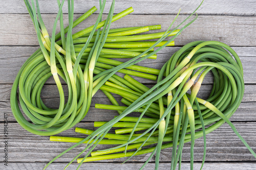 Green stalks of garlic on wooden table. The twisted stems of plants from seed. Preparation of summer salad for healthy diet