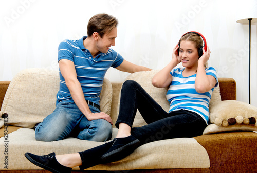 Couple sitting together on sofa. Woman listening music in headphones.