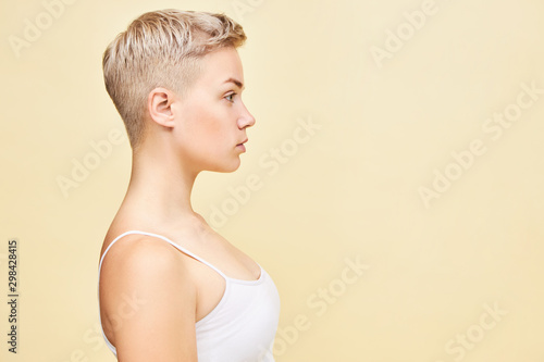 Profile image of beautiful young Caucasian female with boyish pixie haircut, perfect clean skin and athletic body posing in studio. Active lifestyle, sports, health, wellness, beauty people concept