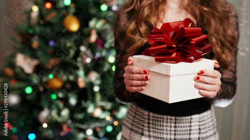 Christmas gift in girl's hands on blinking lights bokeh background. Celebration of winter holidays at home, anazing festive mood and christmas presents for everyone. Woman's hands and gift with photo