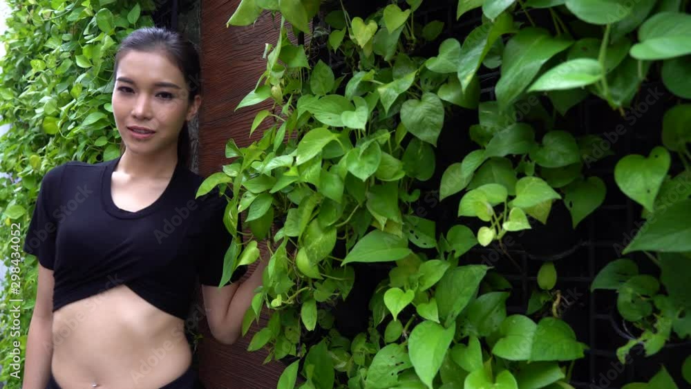 Attractive Asian woman with pierced navel and ponytail posing against an ivy wall - copy space Attractive Asian woman with pierced navel and ponytail posing against an ivy wall - copy space