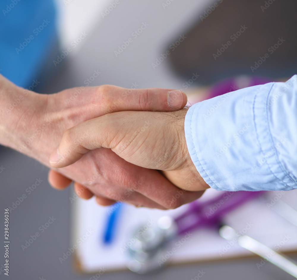 Attractive female doctor shaking a patient's hands in her offic Attractive female doctor shaking a patient's hands in her offic