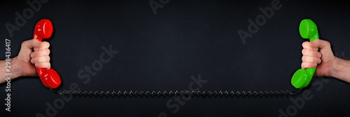 hands with green and red colored old fashioned retro phone reciever with black telephone wire dark slate blackboard background. business problem solution communication support service concept
