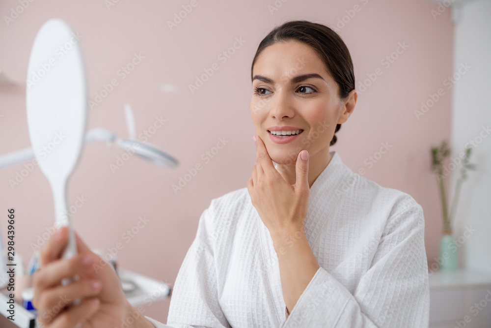 Attractive lady looking in the mirror and touching her face Attractive lady looking in the mirror and touching her face