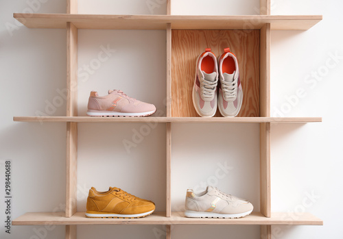 Wooden shelving unit with stylish women's sneakers on white wall