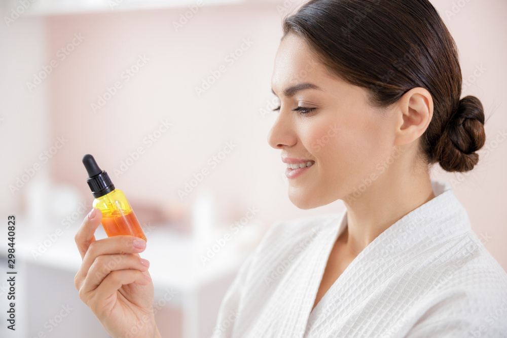 Joyful young woman holding bottle of vitamin serum Joyful young woman holding bottle of vitamin serum