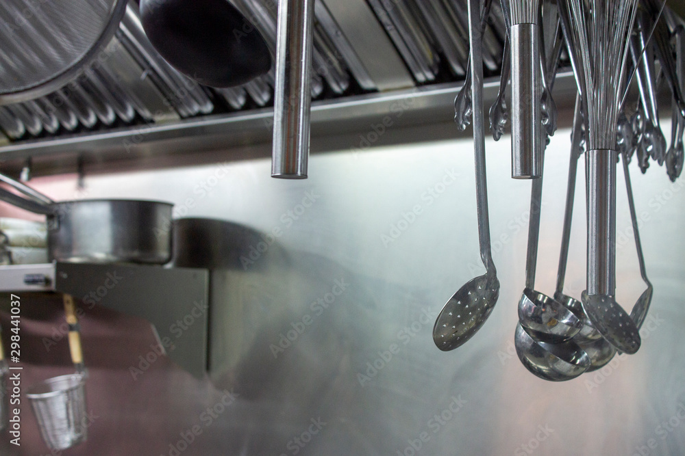 Stainless steel kitchen utensils hanging from the dryer in a professional kitchen. Stainless steel kitchen utensils hanging from the dryer in a professional kitchen.