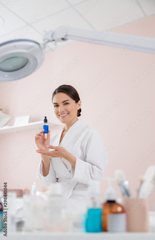 Cheerful young woman holding bottle of serum Cheerful young woman holding bottle of serum