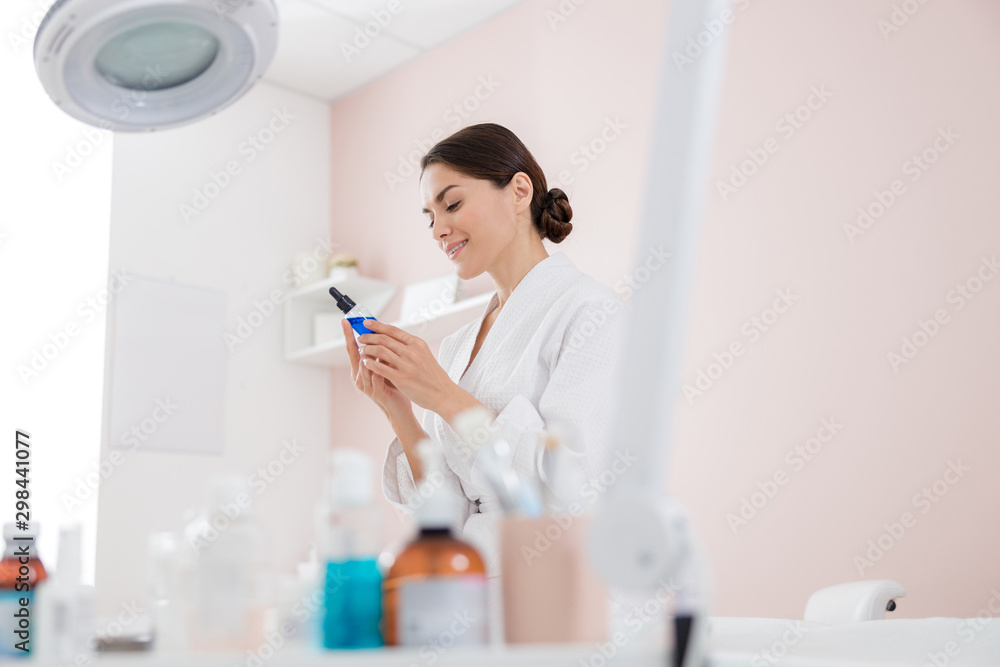 Attractive lady looking at vitamin serum and smiling Attractive lady looking at vitamin serum and smiling