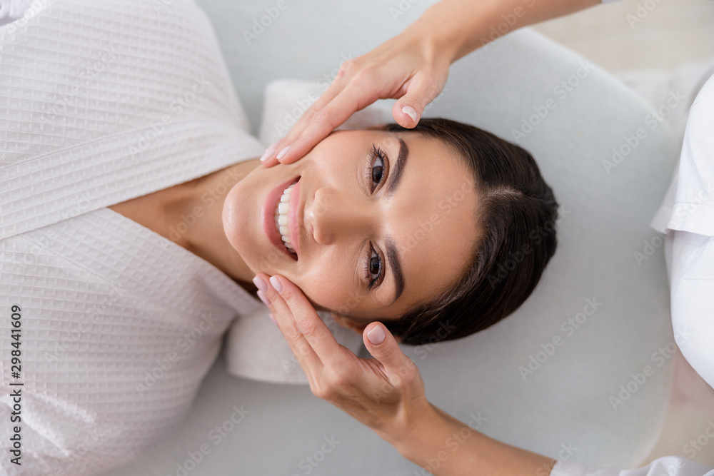 Masseuse hands massaging face of cheerful lady