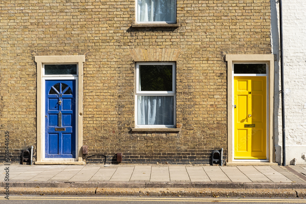 Pair of colourful doors seen on the entrances to old-style terraced houses within a double-yellow road zone. The yellow door has recently been fitted.