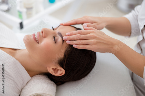 Charming young woman enjoying face massage at beauty salon