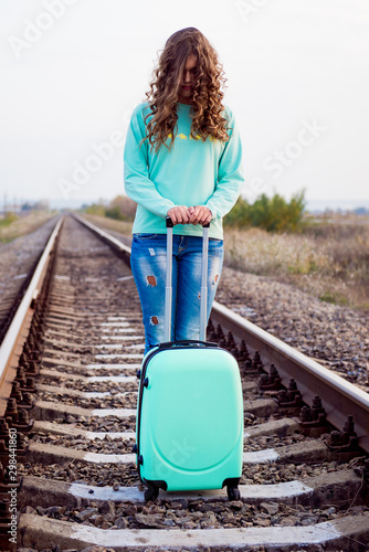 Girl tourist with a suitcase on a railway platform. Autumn train ride. Railway in the fall. Girl with a suitcase by the railway. Turquoise suitcase