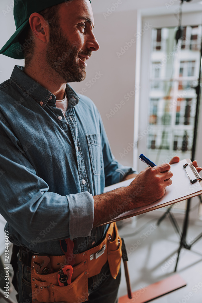 Fototapeta premium Contented construction worker smiling and writing stock photo