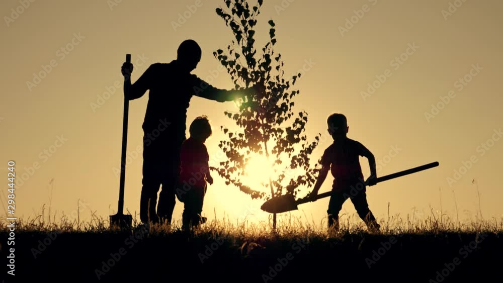A happy family of farmers. Silhouette of a father and two children planting and watering a tree in the Park at sunset.