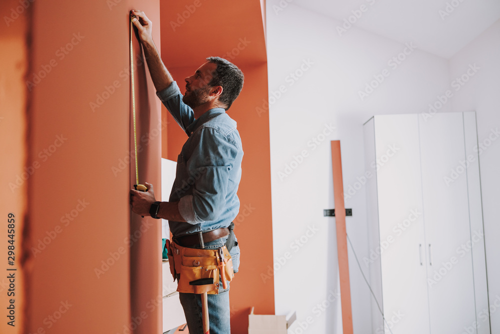 Young bearded handyman is standing near wall