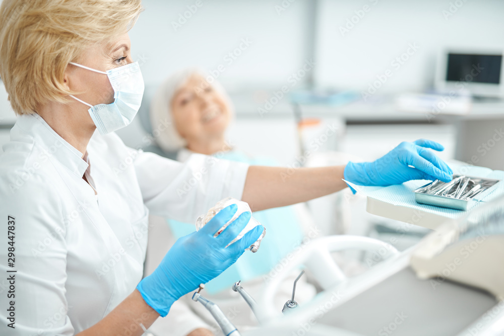 Obraz premium Masked female dentist is taking dental instruments