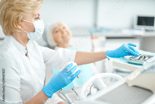 Masked female dentist is taking dental instruments