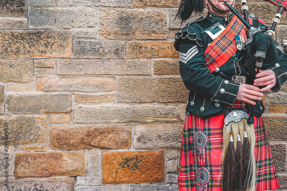 Ταπετσαρία EDINBURGH, SCOTLAND, 24 March 2018 , Scottish bagpiper dressed in traditional red and black tartan dress stand before stone wall