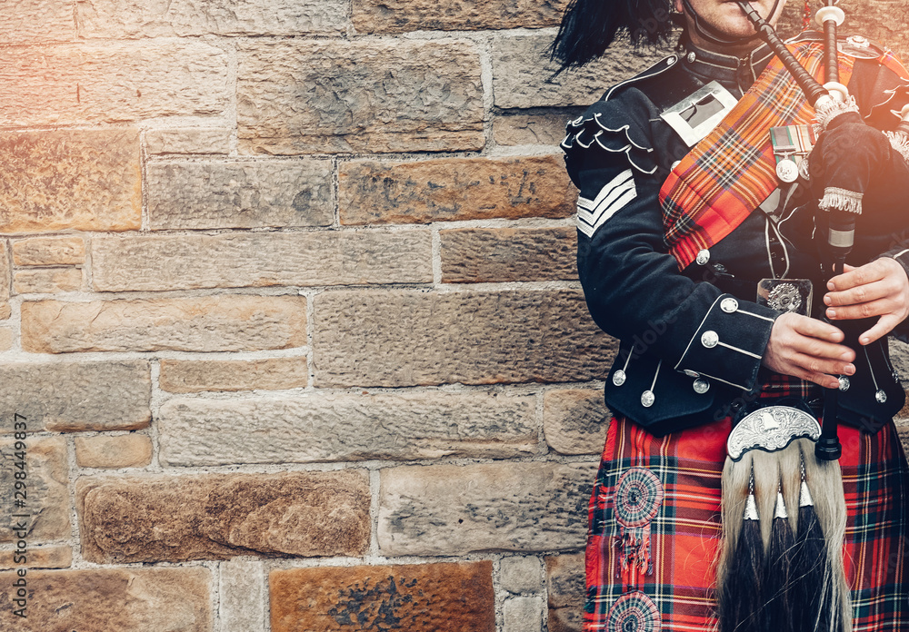 Φωτογραφία EDINBURGH, SCOTLAND, 24 March 2018 , Scottish bagpiper dressed in traditional red and black tartan dress stand before stone wall