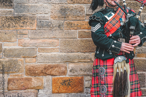 EDINBURGH, SCOTLAND, 24 March 2018 , Scottish bagpiper dressed in traditional red and black tartan dress stand before stone wall. Edinburgh, the most popular tourist city destination in Scotland.. photo