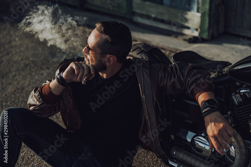 Handsome biker sitting near motorbike and smoking