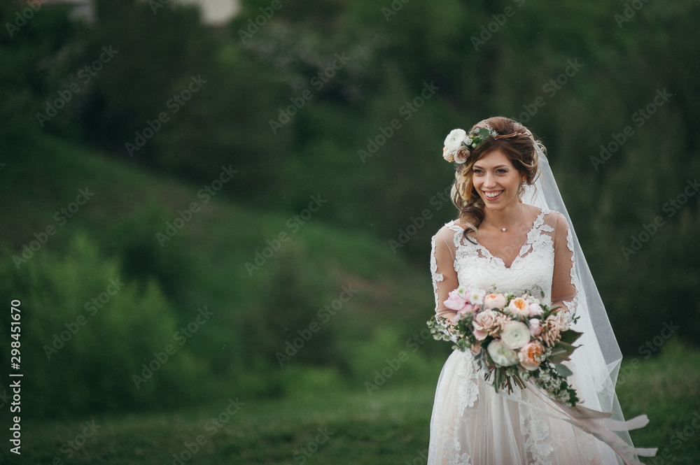 Beautiful bride with fresh flowers in her hair and a bouquet posing on a green field