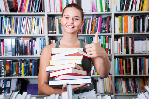 girl holding stack of books shows thump up in a bookstore shows thump up