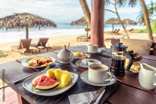 Fototapeta Naklejka Na Ścianę i Meble -  Breakfast on sea beach in Sri Lanka. Table setting with vegan food and coffee in restaurant outdoor. Buffet with exotic fruits on ocean coast. Concept of travel and vacation in tropical resort.