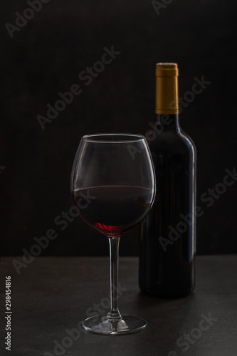 Wine bottle with Bordeaux glass on the black background. Luxury wine tasting concept.