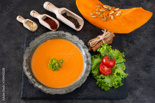Pumpkin cream soup with tomato and spices on the black table background