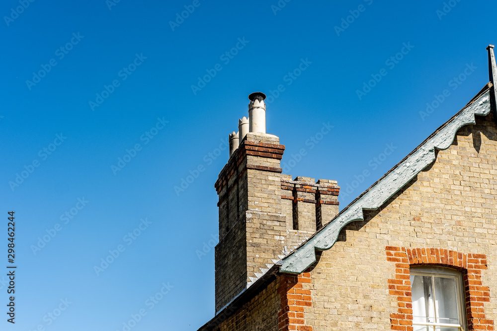 Fine detailed view of old, multiple chimneys seen atop an old, brick built house. Cowlings are fitted to the chimneys to prevent birds nesting. Fine detailed view of old, multiple chimneys seen atop an old, brick built house. Cowlings are fitted to the chimneys to prevent birds nesting.