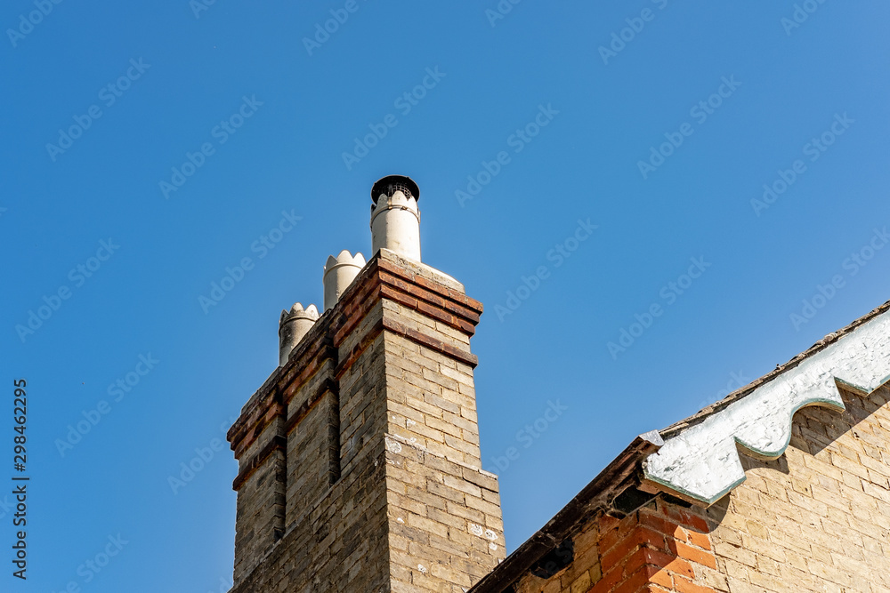 Fine detailed view of old, multiple chimneys seen atop an old, brick built house. Cowlings are fitted to the chimneys to prevent birds nesting.