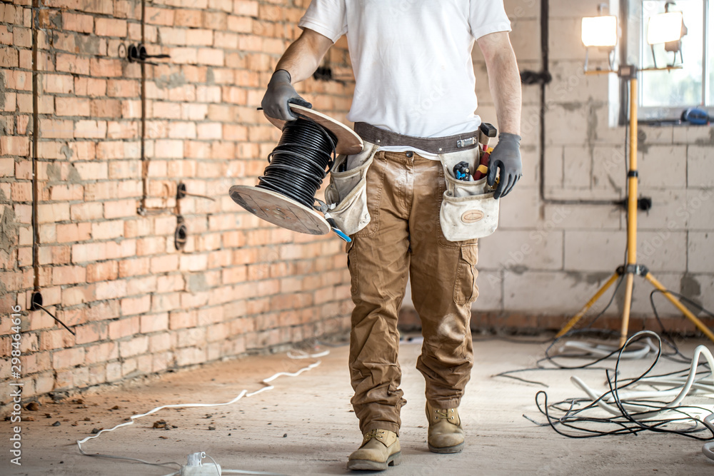 Electrician with tools, working on a construction site. Repair and handyman concept. - obrazy, fototapety, plakaty 