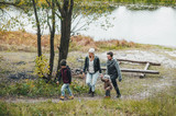 Mom, dad and little childrens, walking on autumn forest near river. They are talking and enjoying beautiful autumn day.