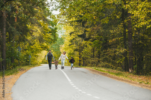 Mom  dad and little childrens  walking on country road. They are talking and enjoying beautiful autumn day.
