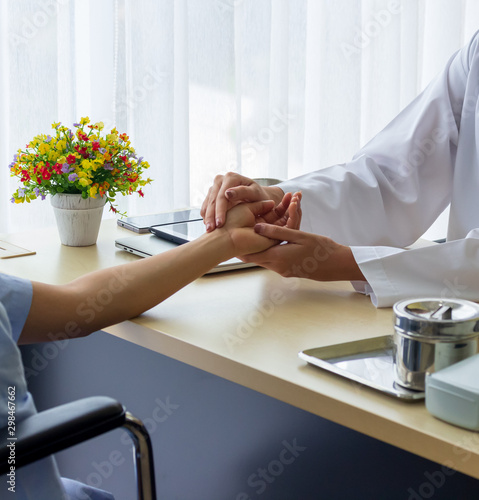 Beautiful female doctor holding patient's hand for encouragement and empathy and touching her arm. Partnership, trust and medical ethics concept. Bad news lessening and support. Patient cheering