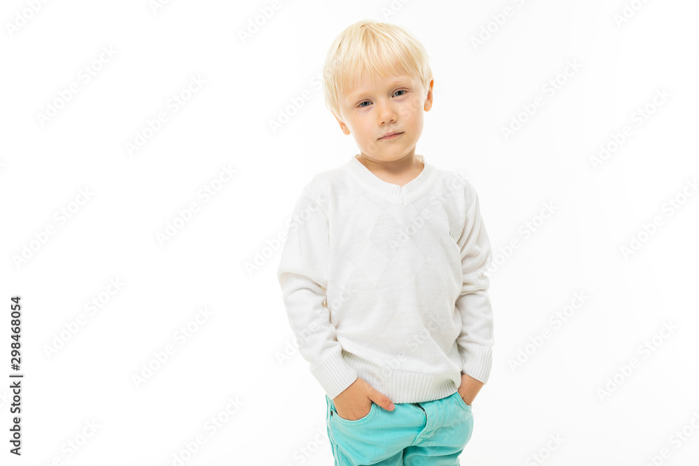 Little boy with short blonde hair, blue eyes, cute appearance, in white jacket, light blue pants, standing with his hands in his pockets Little boy with short blonde hair, blue eyes, cute appearance, in white jacket, light blue pants, standing with his hands in his pockets