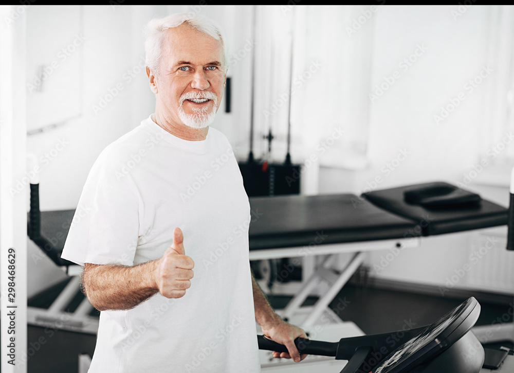Senior man showing thumbs up while training at wellness center Senior man showing thumbs up while training at wellness center
