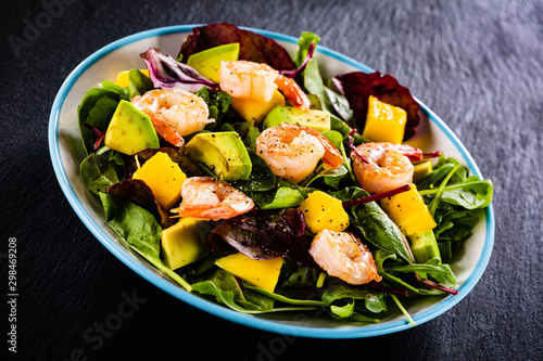 Salad with shrimps on black stone plate