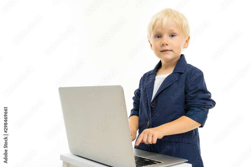 Little boy with short blonde hair, blue eyes, cute appearance, in white jacket, grey pants, blue jocket, standing with laptop and typing Little boy with short blonde hair, blue eyes, cute appearance, in white jacket, grey pants, blue jocket, standing with laptop and typing