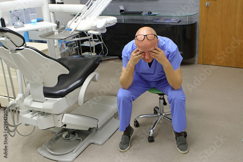 Tired mature dentist with eyes problem. Having short break for regeneration after long working hours in his office photo