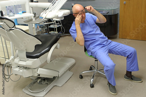 Tired mature dentist with eyes problem. Having short break for regeneration after long working hours in his office
