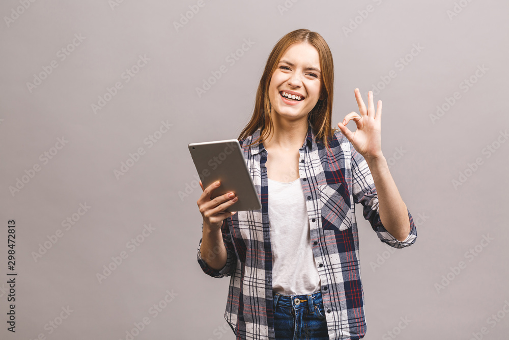 Attractive smiling girl in casual using tablet showing okay sign. Woman with tablet pc, isolated on grey background. Attractive smiling girl in casual using tablet showing okay sign. Woman with tablet pc, isolated on grey background.