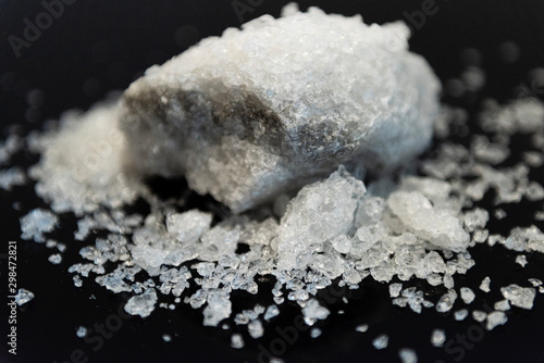 Large crystal of salt on black reflective surface  selective focus  natural edible salt © Oana