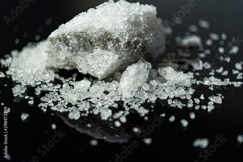 Large crystal of salt on black reflective surface; selective focus; natural edible salt