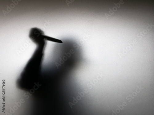 Halloween concept. Blurred shadow of hand holding sharp knife behind white mirror background. Murder scene.